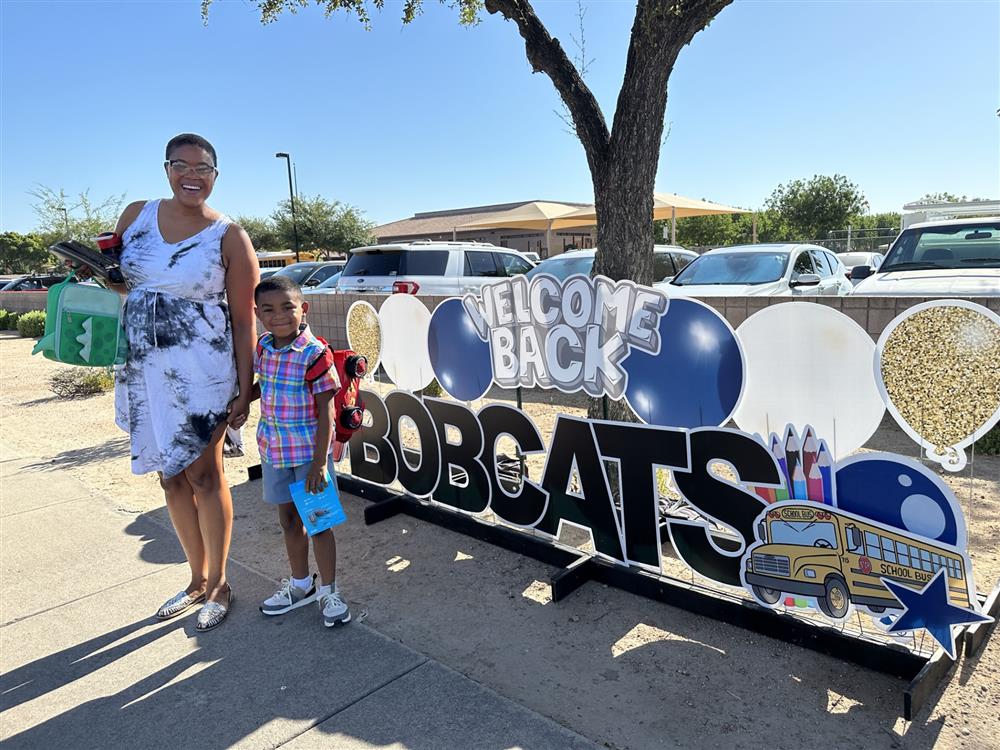 A family smiles next to a sign at Basha Elementary School that says \