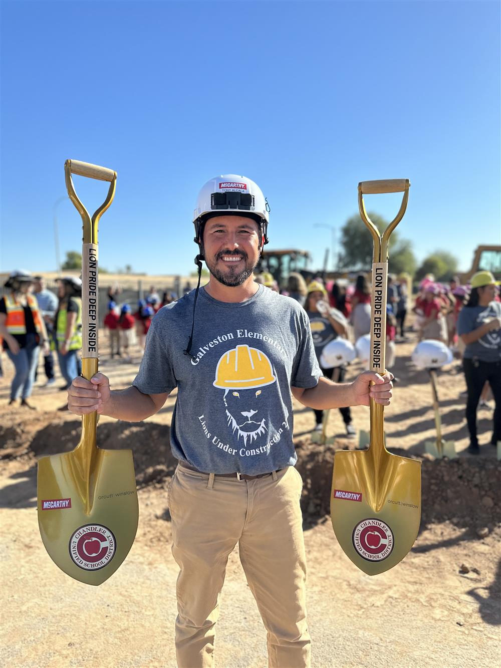 Galveston Elementary School principal Tony Alcala wears a construction hard hat while holding two gold shovels