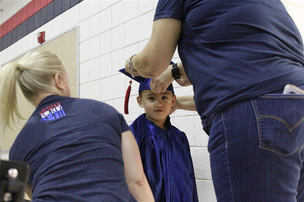 Teachers help a kindergarten student with his cap and gown