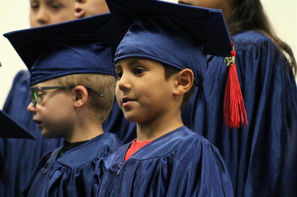 A kindergarten student is wearing a cap and gown