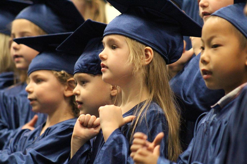 A kindergarten student is wearing a cap and gown