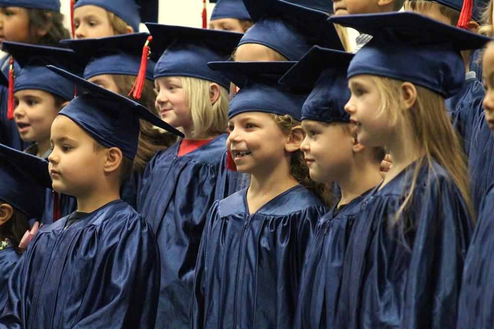 A kindergarten student is wearing a cap and gown