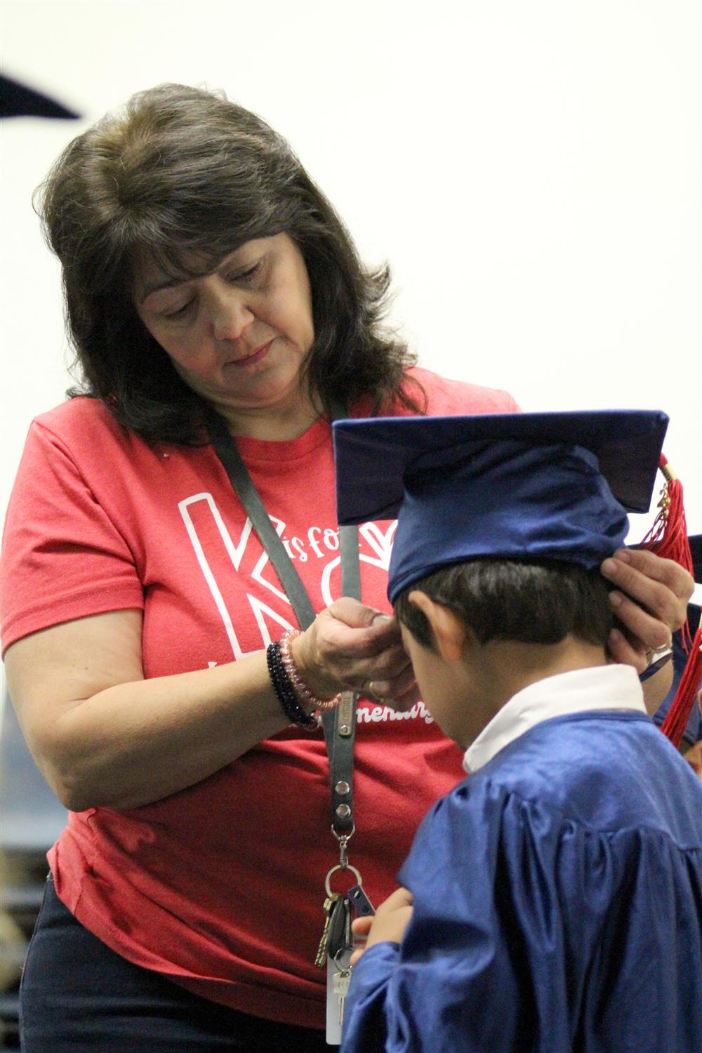 A teacher wearing a red shirt adjusts a student's graduation cap