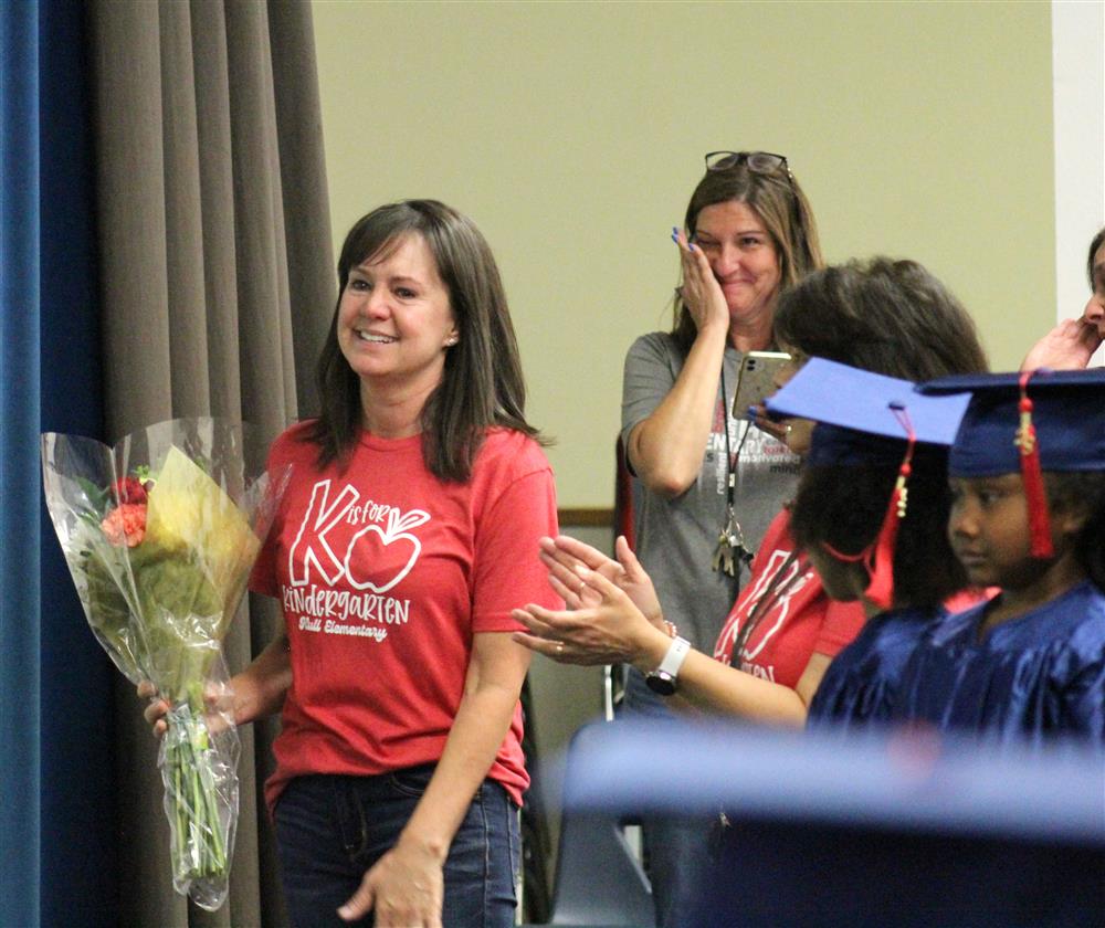 A teacher holds flowers in her hands as another teacher wipes away a tear