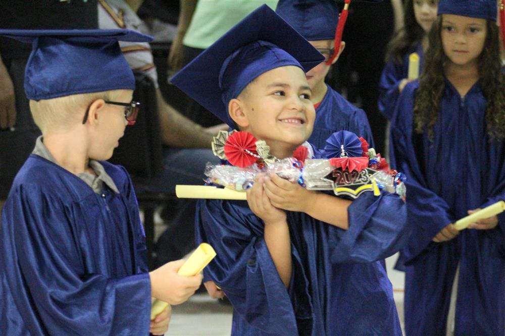 A graduating kindergarten student is wearing a wreath of goodies around his neck