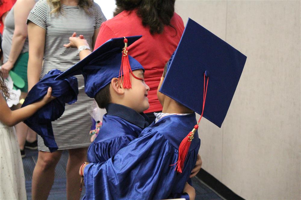 Two boys give each other a hug. They're dressed in caps and gowns