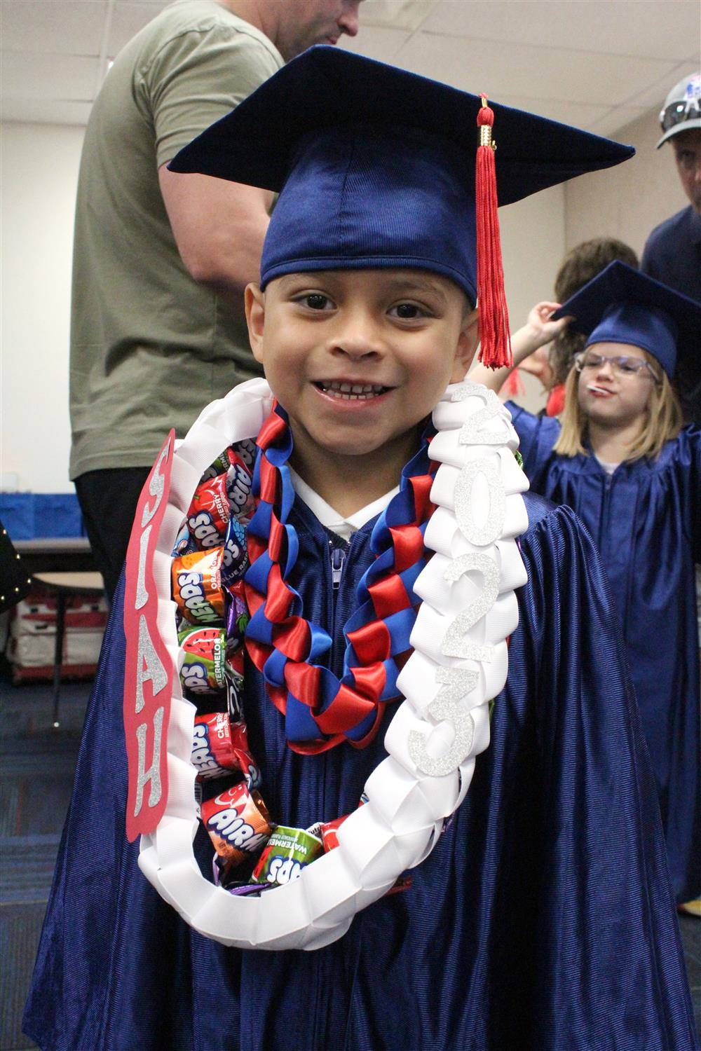 A student smiles for the camera wearing a cap, gown, and wreath of goodies