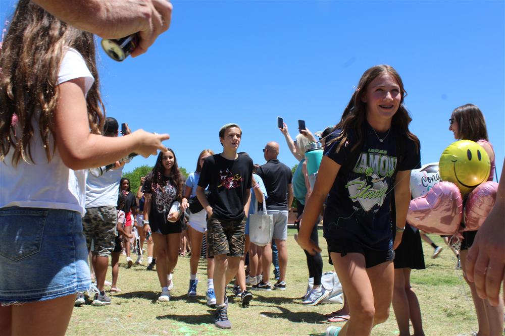 Students walk through a tunnel of parents with silly string