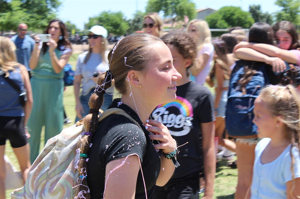 A girl walks through a tunnel of parents with silly string