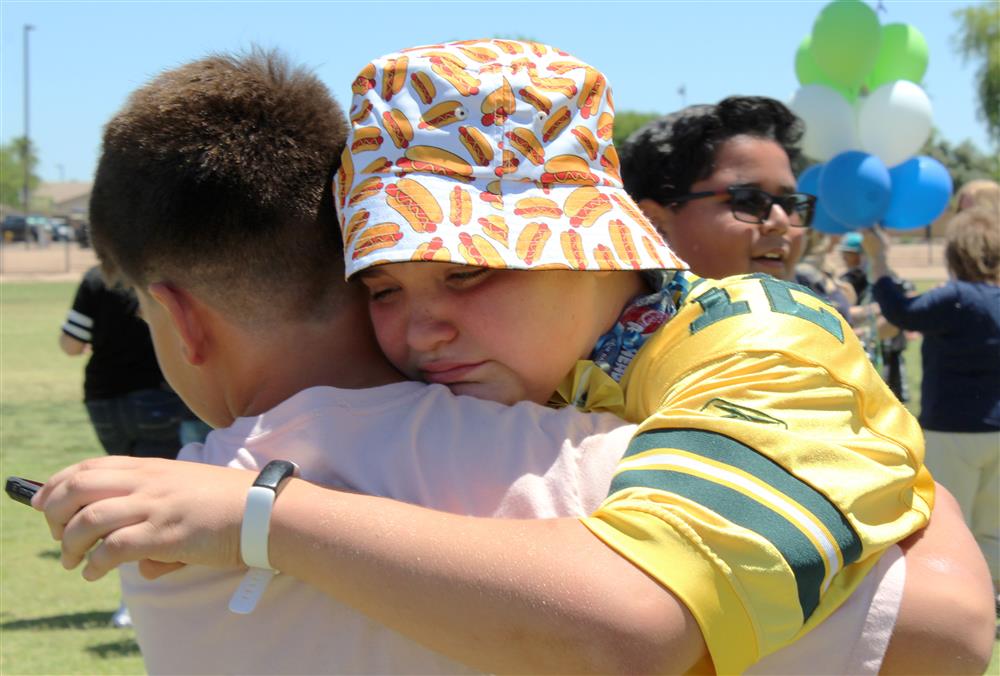 An emotional student wearing a hot-dog printed hat hugs his friend 