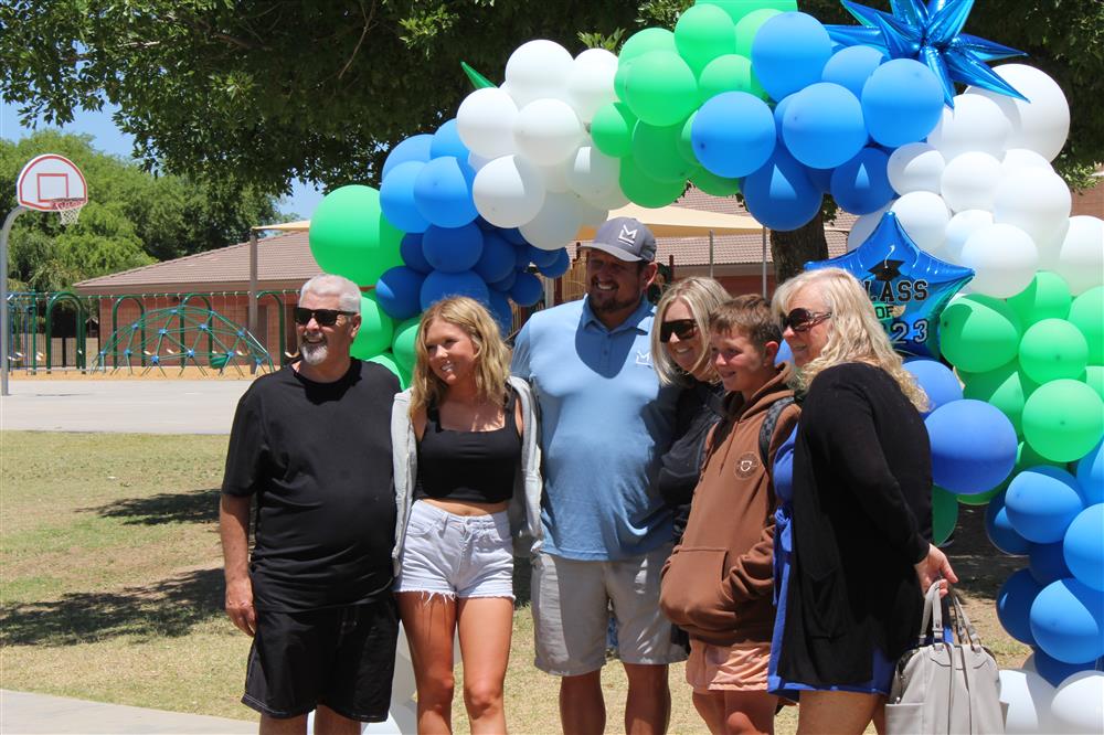 A family poses for a photo with a blue, green, and white balloon arch behind them