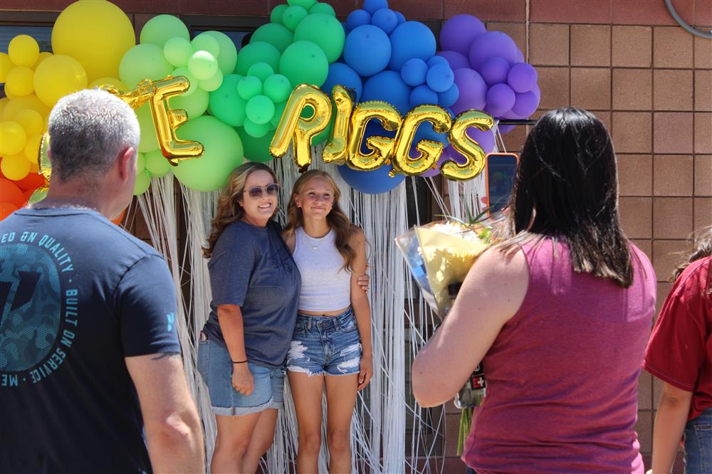 A family poses for a photo with a rainbow balloon arch behind them