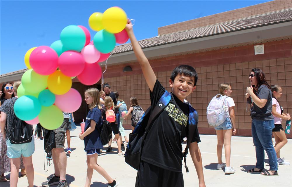 A student holds a string attached to a cluster of colorful balloons from an arch